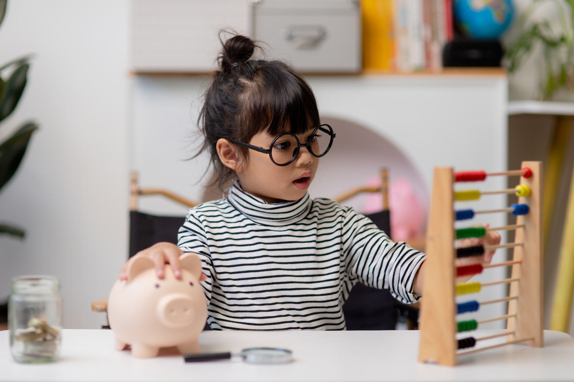 Little Asian girl saving money in a piggy bank, learning about saving, Kid save money for future